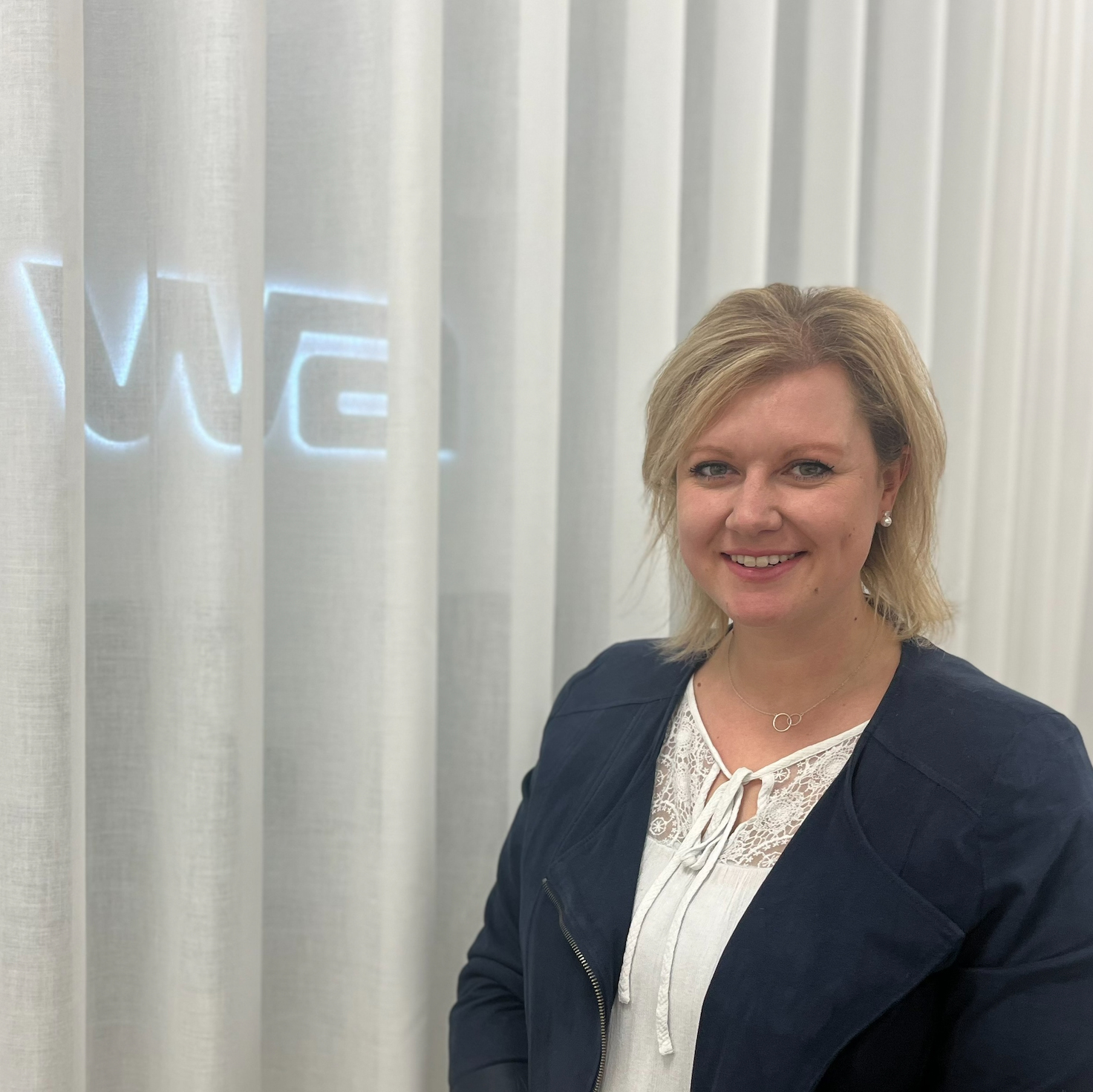 Frau mit blonden Haaren vor weißem Vorhand