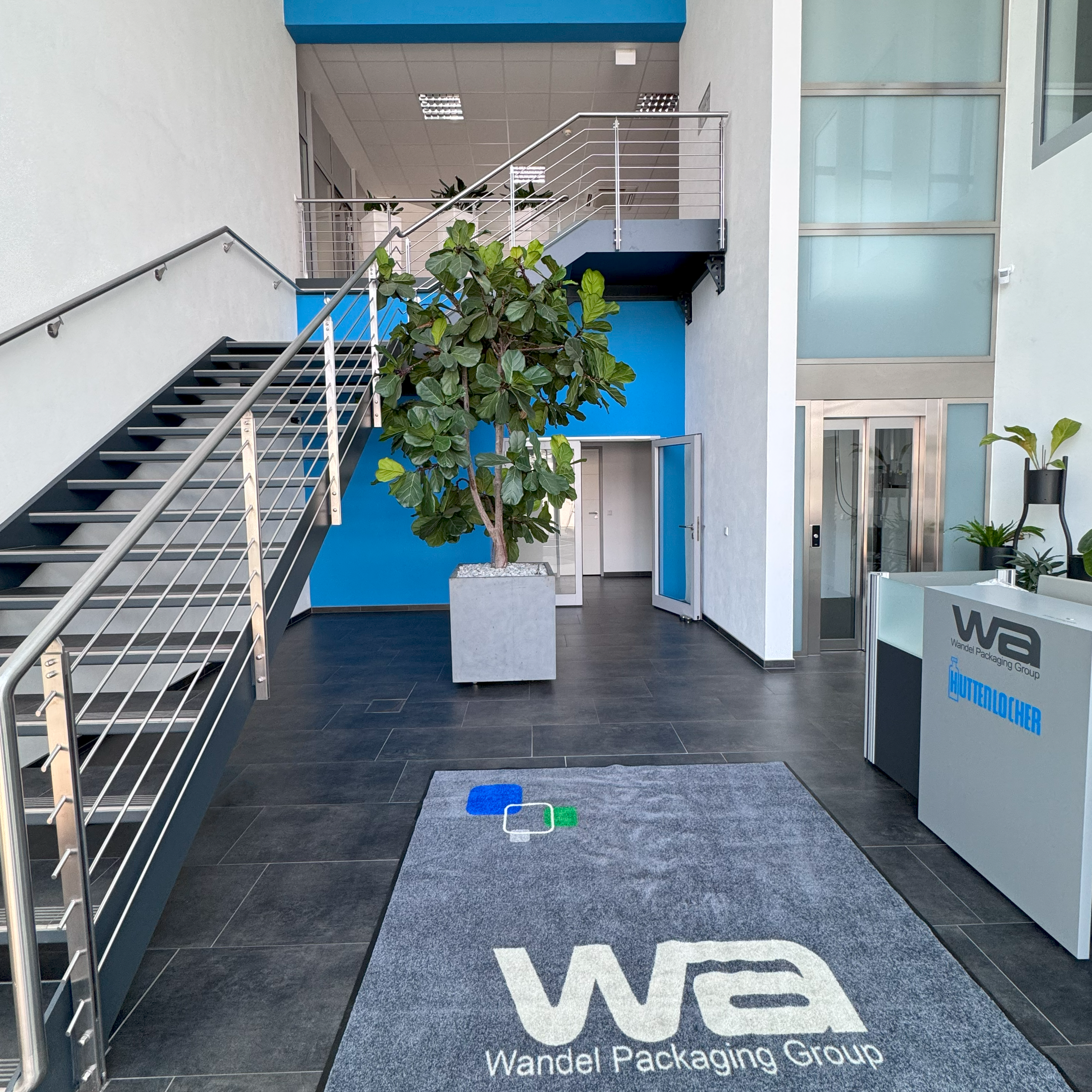 Eingangsbereich Neckartailfingen. Teppich mit Logo, Treppe links führ in zweiten Stock.