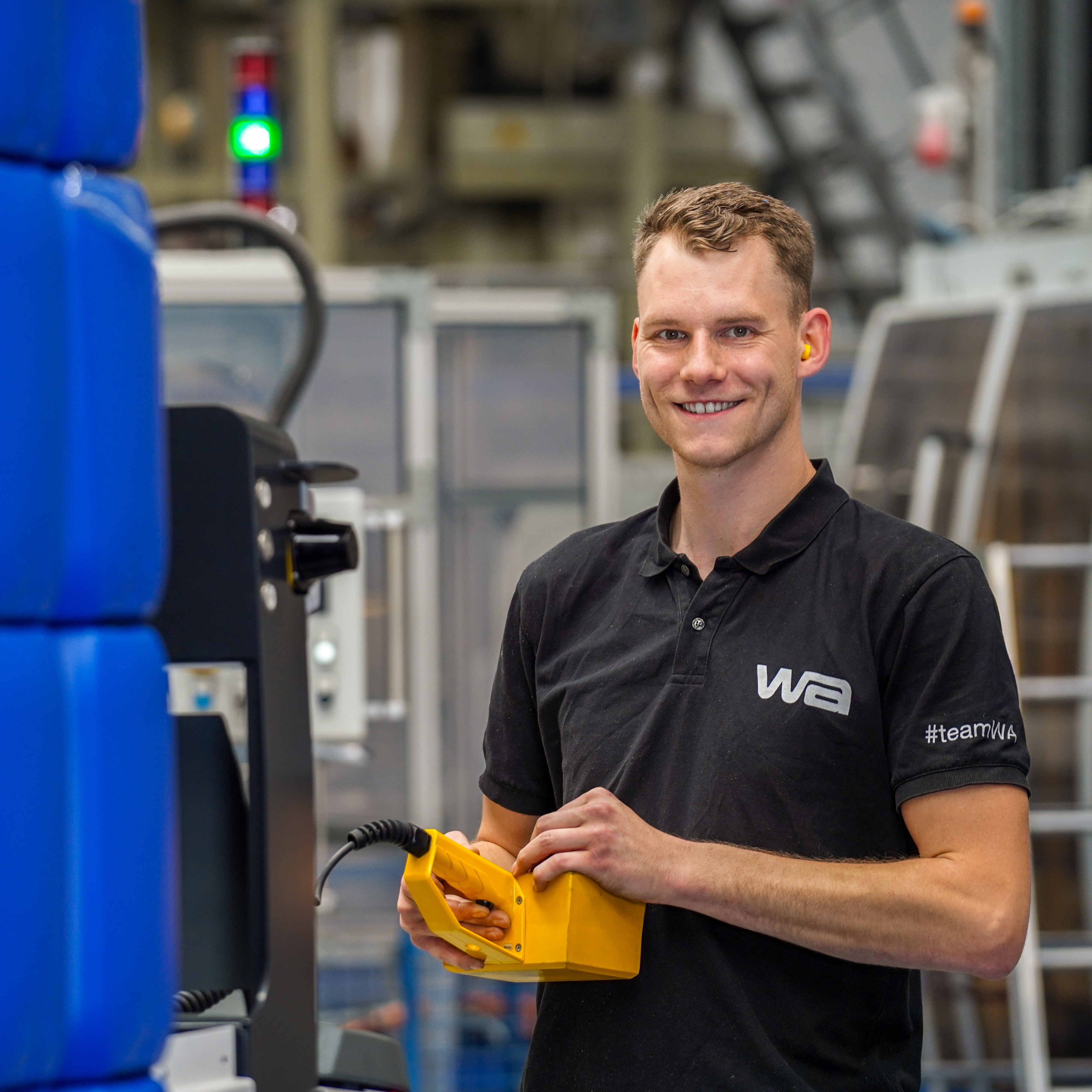 #teamWA Mitarbeiter mit Steuergerät in der Hand steht neben stapelbaren Kanister